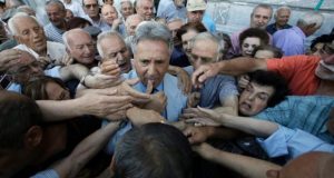 Un employé de la Banque Nationale de Grecque distribue des billets prioritaires pour les retraités faisant la queue devant une succursale bancaire dans le centre d'Athènes.