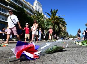 A family walks by flowers placed near stains on the pavement on la Promenade des Anglais in tribute to the victims of the deadly Bastille Day attack in Nice, on July 16, 2016. The Islamic State group claimed responsibility for the truck attack that killed 84 people in Nice on France's national holiday, a news service affiliated with the jihadists said on July 16. Tunisian Mohamed Lahouaiej-Bouhlel, 31, smashed a 19-tonne truck into a packed crowd of people in the Riviera city celebrating Bastille Day -- France's national day. / AFP PHOTO / GIUSEPPE CACACE